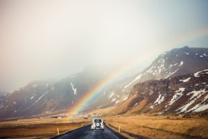 white antique car on mountain road under rainbow