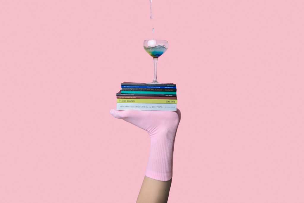 a small stack of books and a wine glass are balanced on the upward-facing sole of apink-socked foot